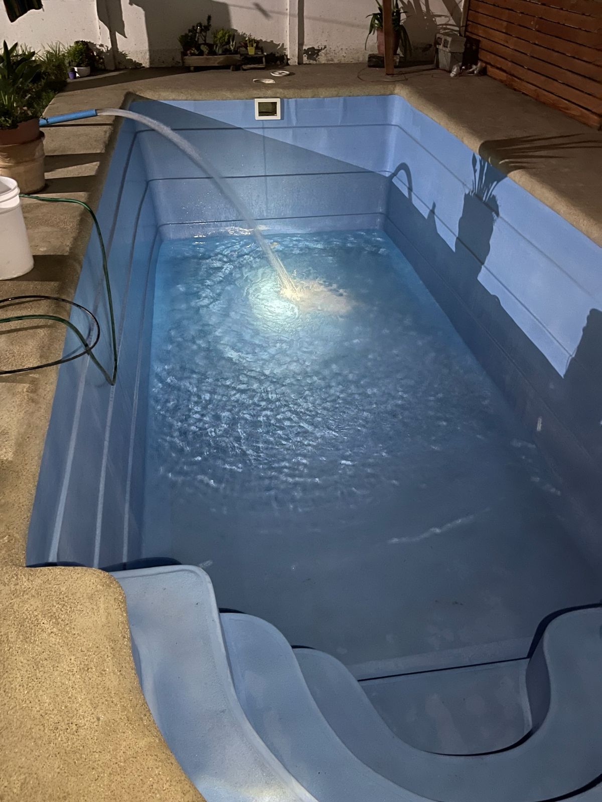 Piscina fibra de vidrio azul llenándose de noche con iluminación interior