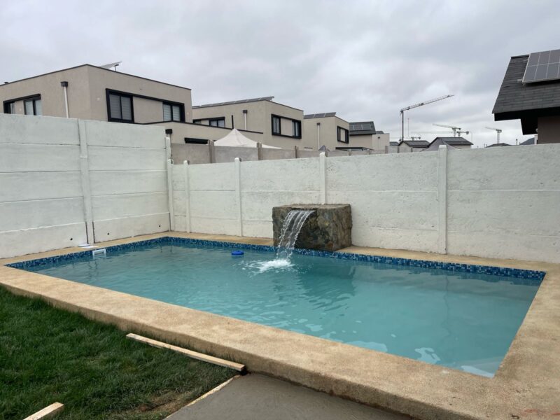 Piscina rectangular con fuente de roca volcánica y mosaico azul eléctrico