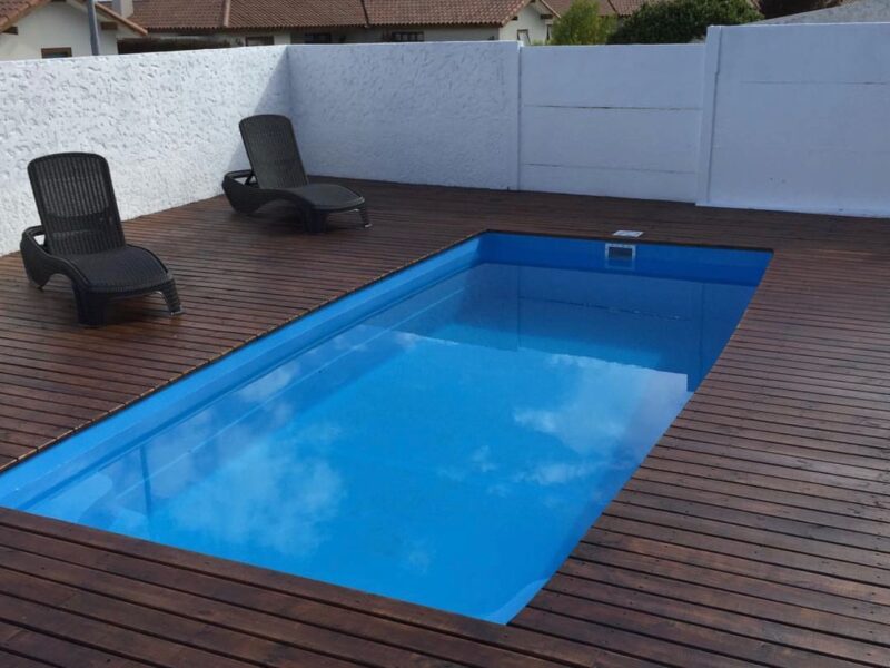 Piscina rectangular con deck de madera y postes rústicos, vista al mar