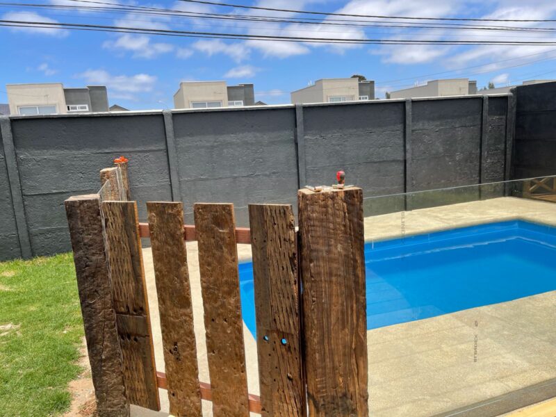 Piscina rectangular con deck de madera y jardín, vista al mar
