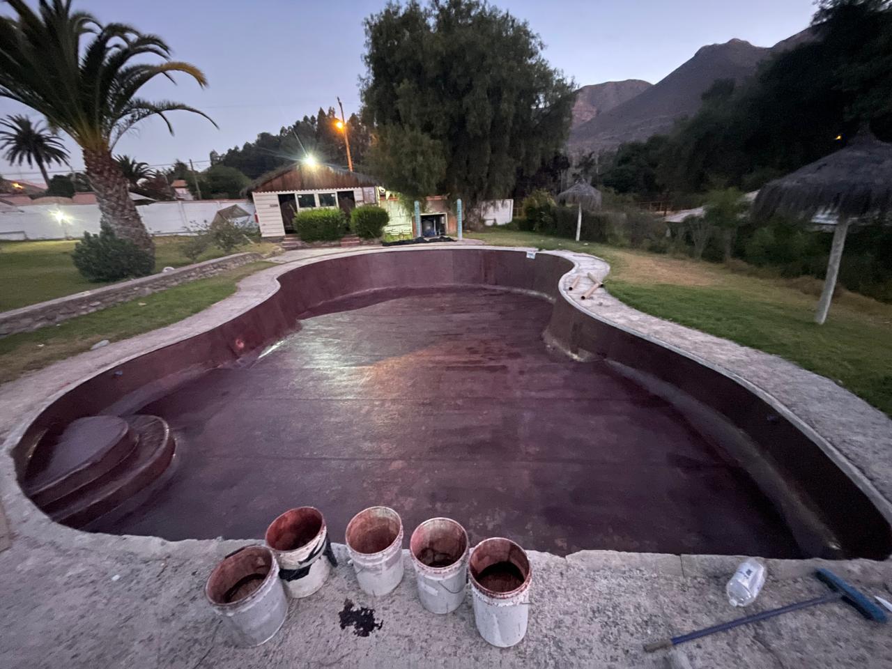 Aplicación de resina en piscina grande, vista nocturna con montañas al fondo